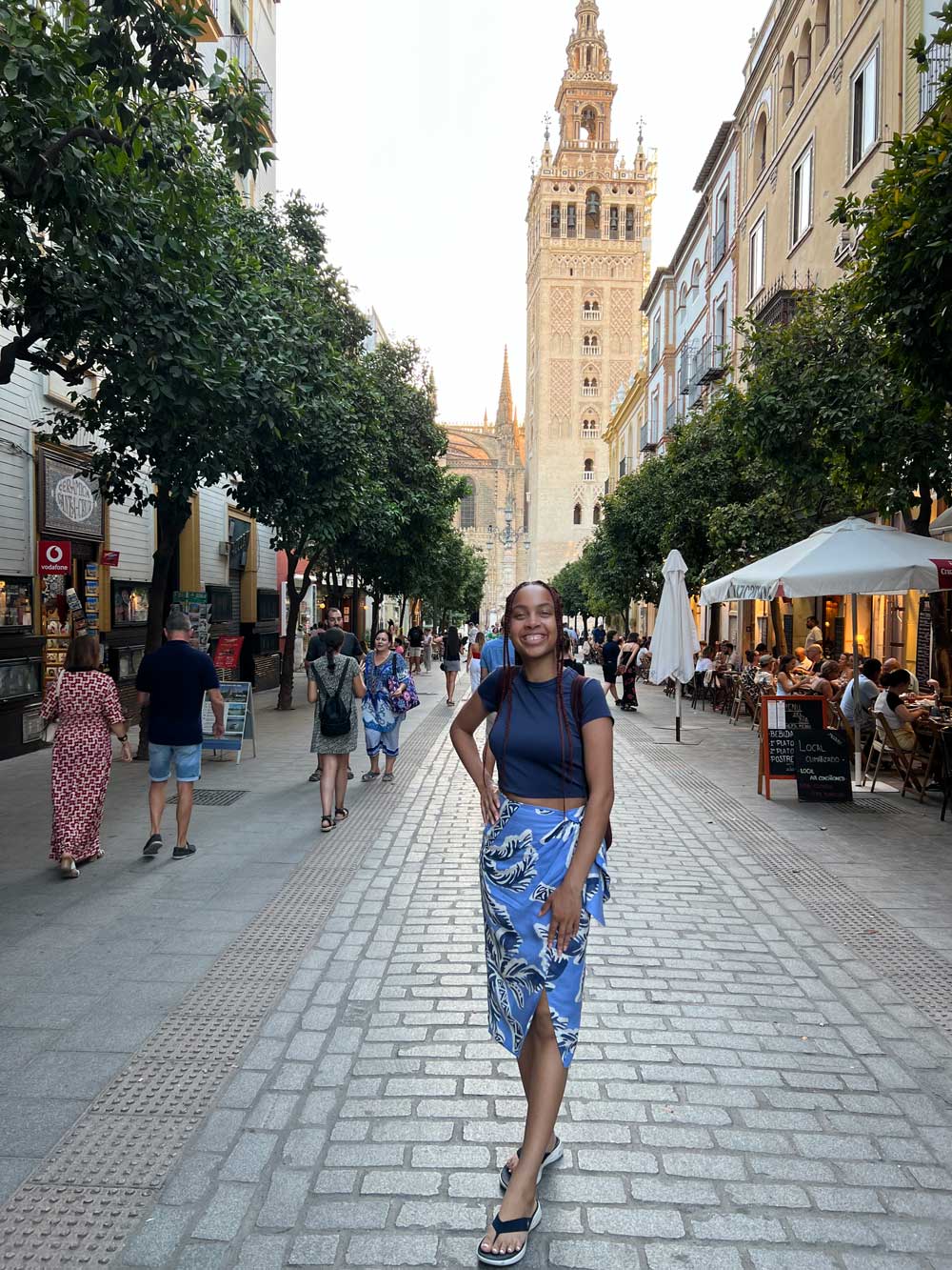 Kameron smiling in a blue floral skirt in front of La Giralda in Seville